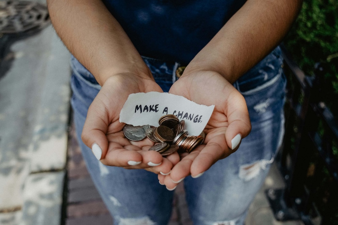 Hands holding a piece of paper with 'MAKE A CHANGE' surrounded by coins.